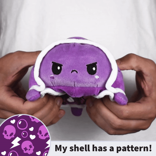 Someone flips a TeeTurtle Reversible Turtle Plushie (Punk Shell) from an angry, purple turtle with a patterned shell to a smiling, pink one. Text says