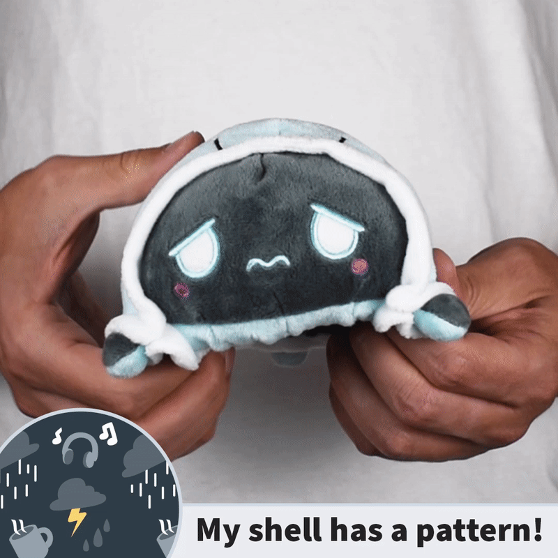 A person holds a TeeTurtle Reversible Turtle Plushie (Rainy Day Shell) featuring a sad expression and hood. Below, the text proclaims, "My shell has a pattern!" In the corner, there's a cartoon cloud icon depicting rain, lightning, and headphones—highlighting the plushie's versatile expressions.