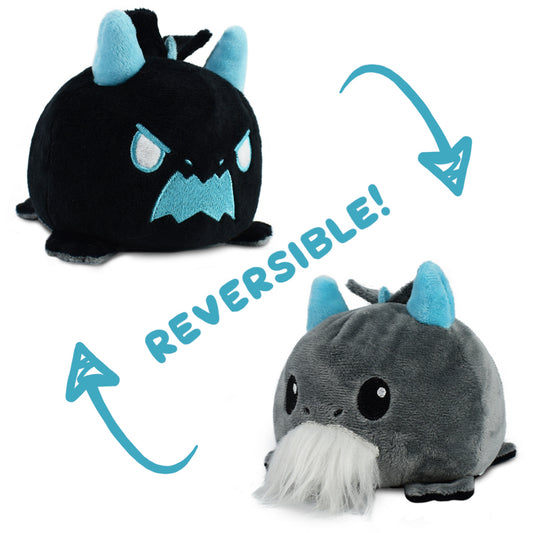 A TeeTurtle Reversible Dragon Plushie (Beard) by TeeTurtle, featuring one side as an angry black dragon with blue ears and the other side as a happy gray dragon with a white beard and blue ears. Arrows emphasize the reversible feature of this mood plushie.